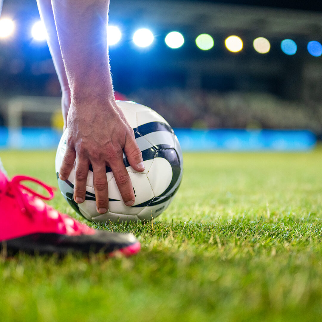 Soccer player putting sports ball on field grass close up