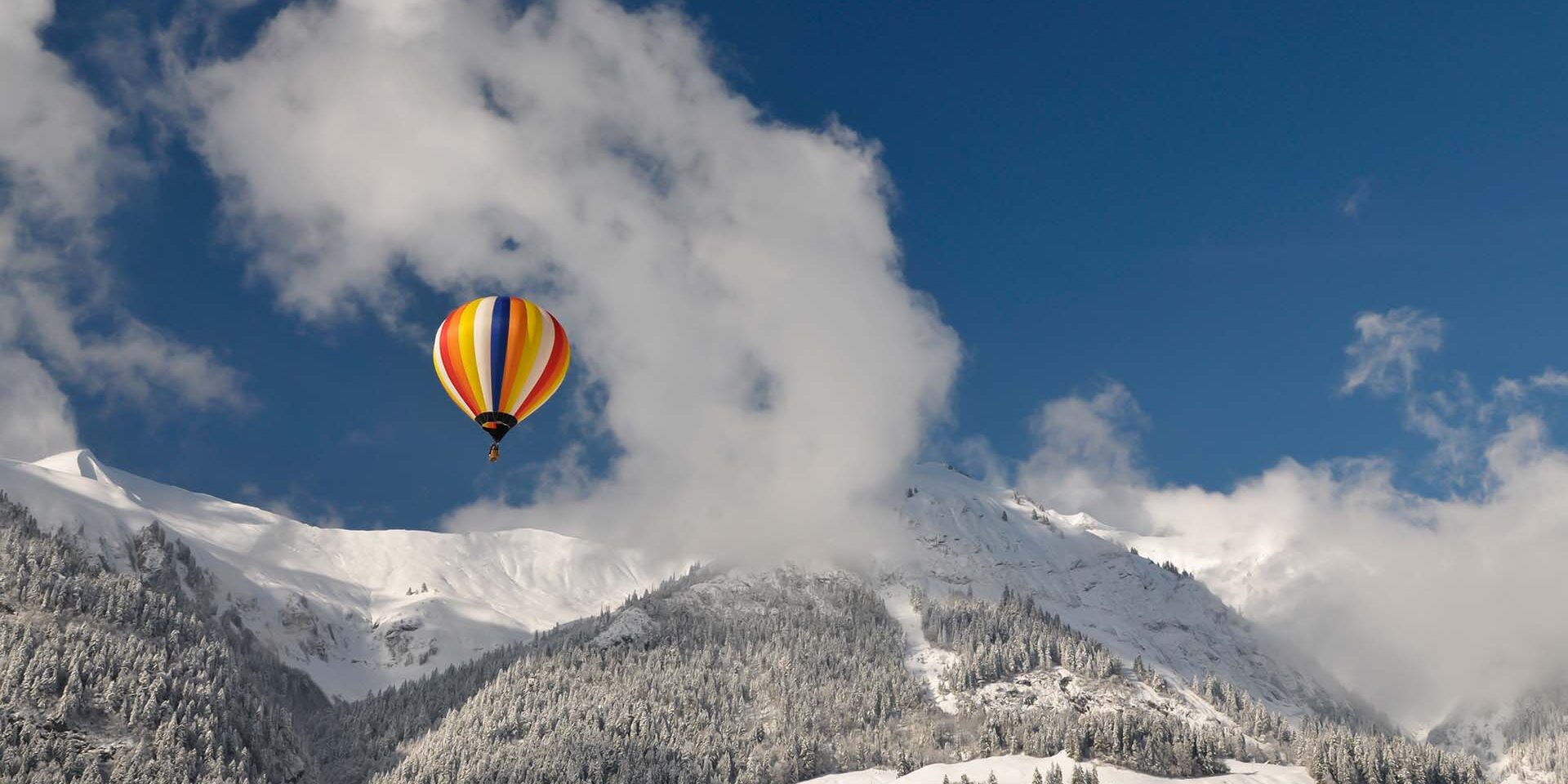 Hot-Air Balloon and snow-covered Mountains Colored hot-air balloon against blue sky with clouds. Snow-covered landscape in the Swiss Alps near Chateau-d'Oex.