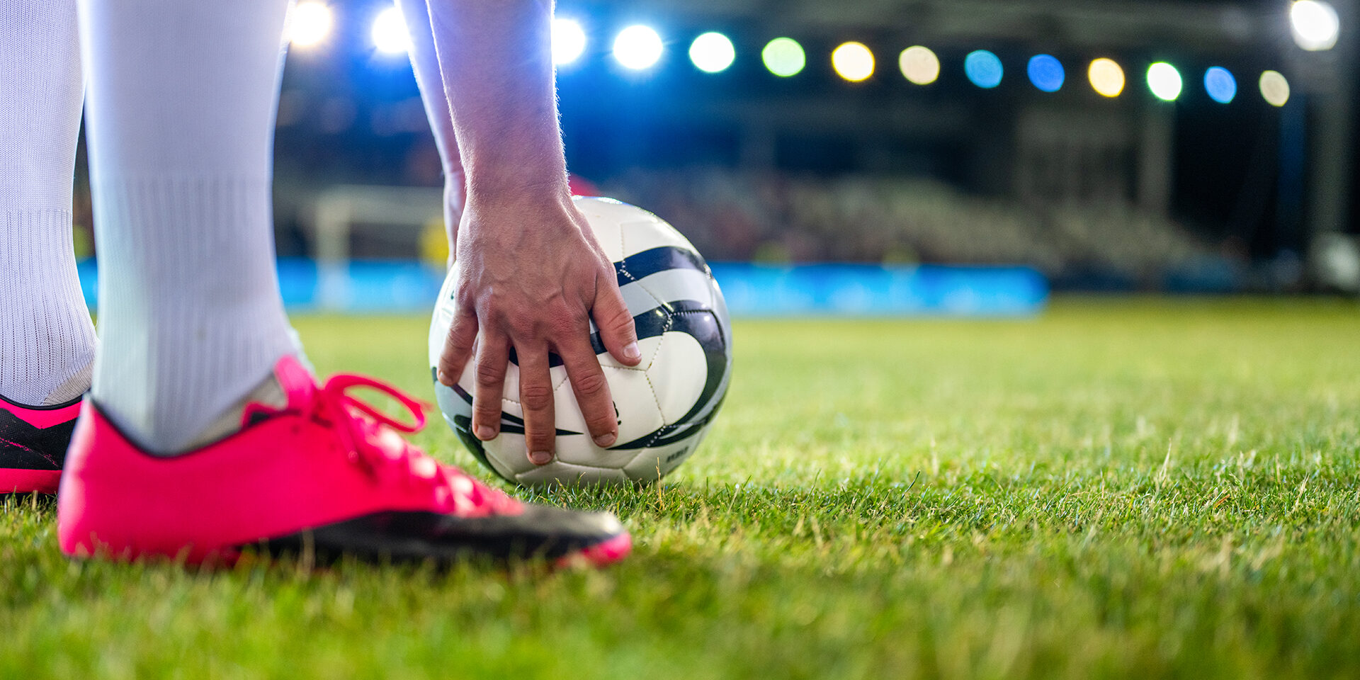 Soccer player putting sports ball on field grass close up